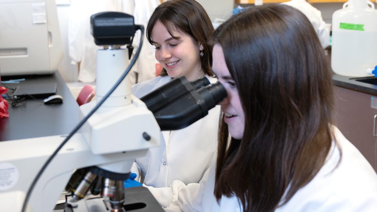 两个穿着实验服的女学生凝视着显微镜