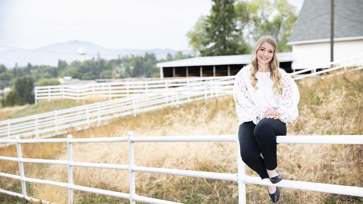 一个女人坐在白色的篱笆上，背景是一个白色的谷仓.