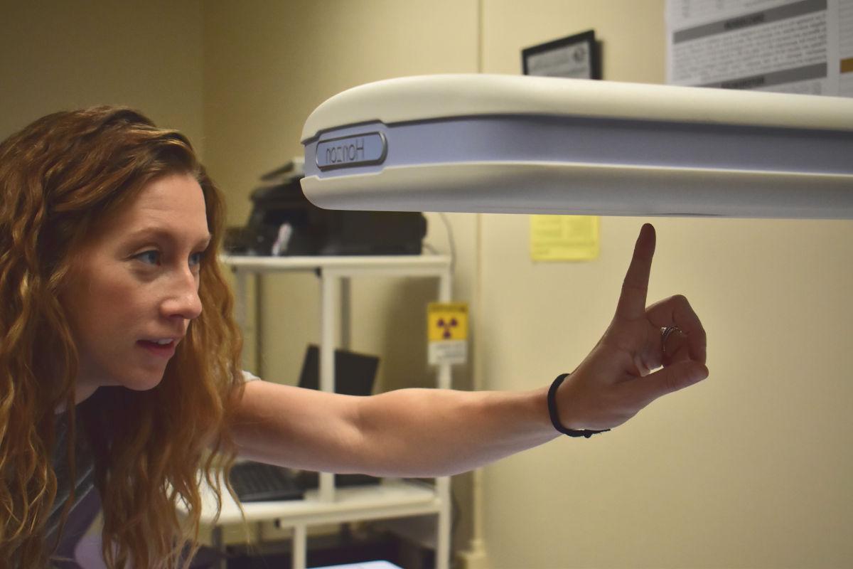 Ann Brown points at a portion of the dual-energy X-ray absorptiometry machine in the Human Performance Lab.